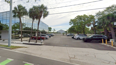 A sunny day at a serene office park in Tampa with reflective glass facade, palm trees lining the street, and a parking lot filled with cars.