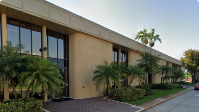 Modern office building in Kendall, Miami, with large windows flanked by lush palm trees on a clear day.